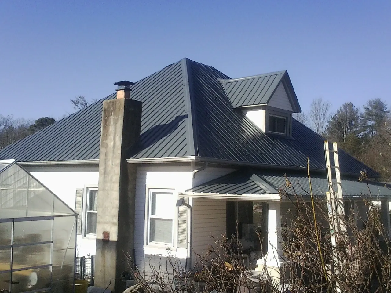 Dark blue standing seam metal roof on a white farmhouse with dormer — Slate & Tile Roof Repair by Roofing Brothers in Forest
