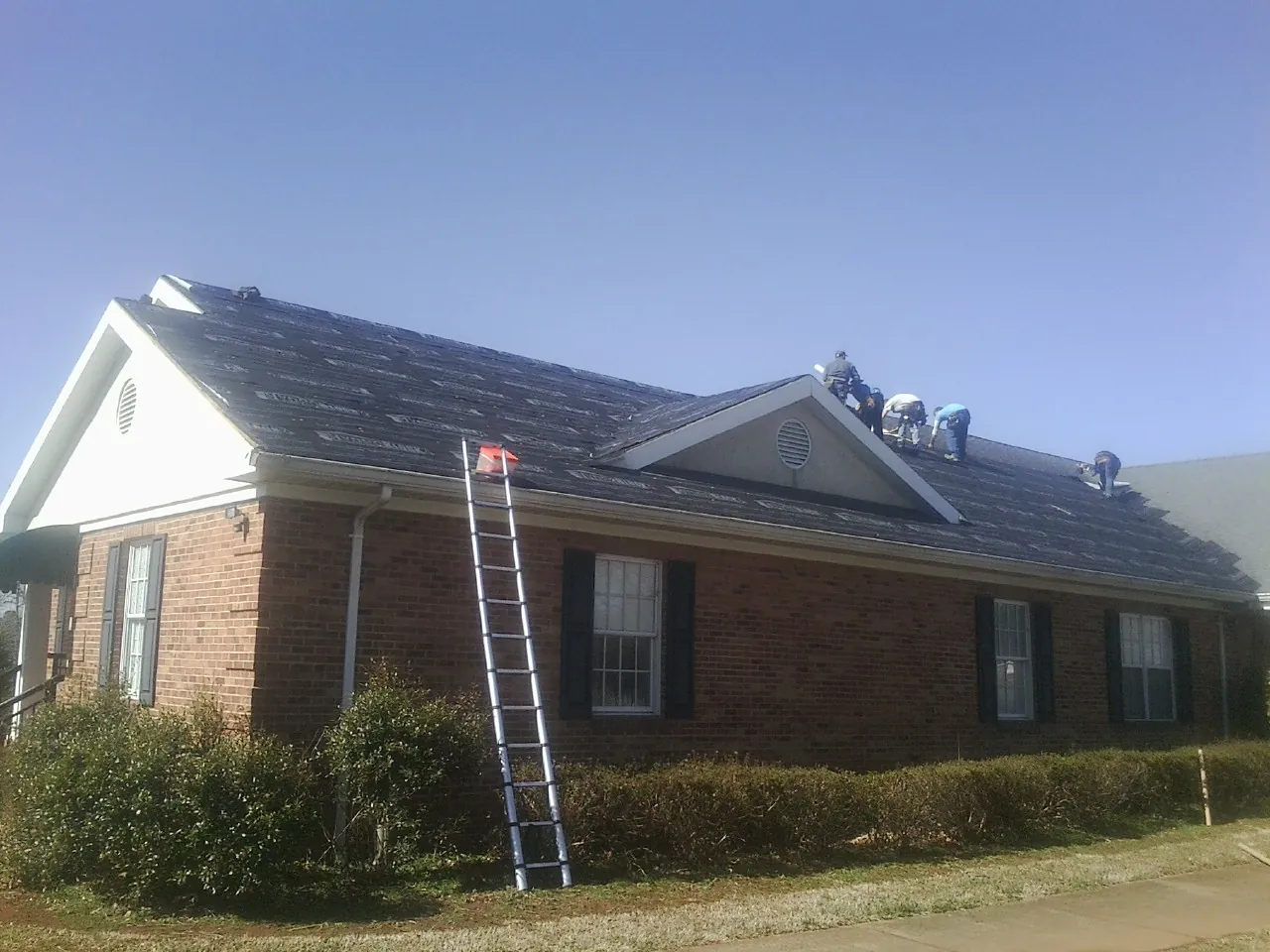 Crew tearing shingles off a brick ranch roof with a ladder set — Emergency Roof Repair work by our crew in Forest