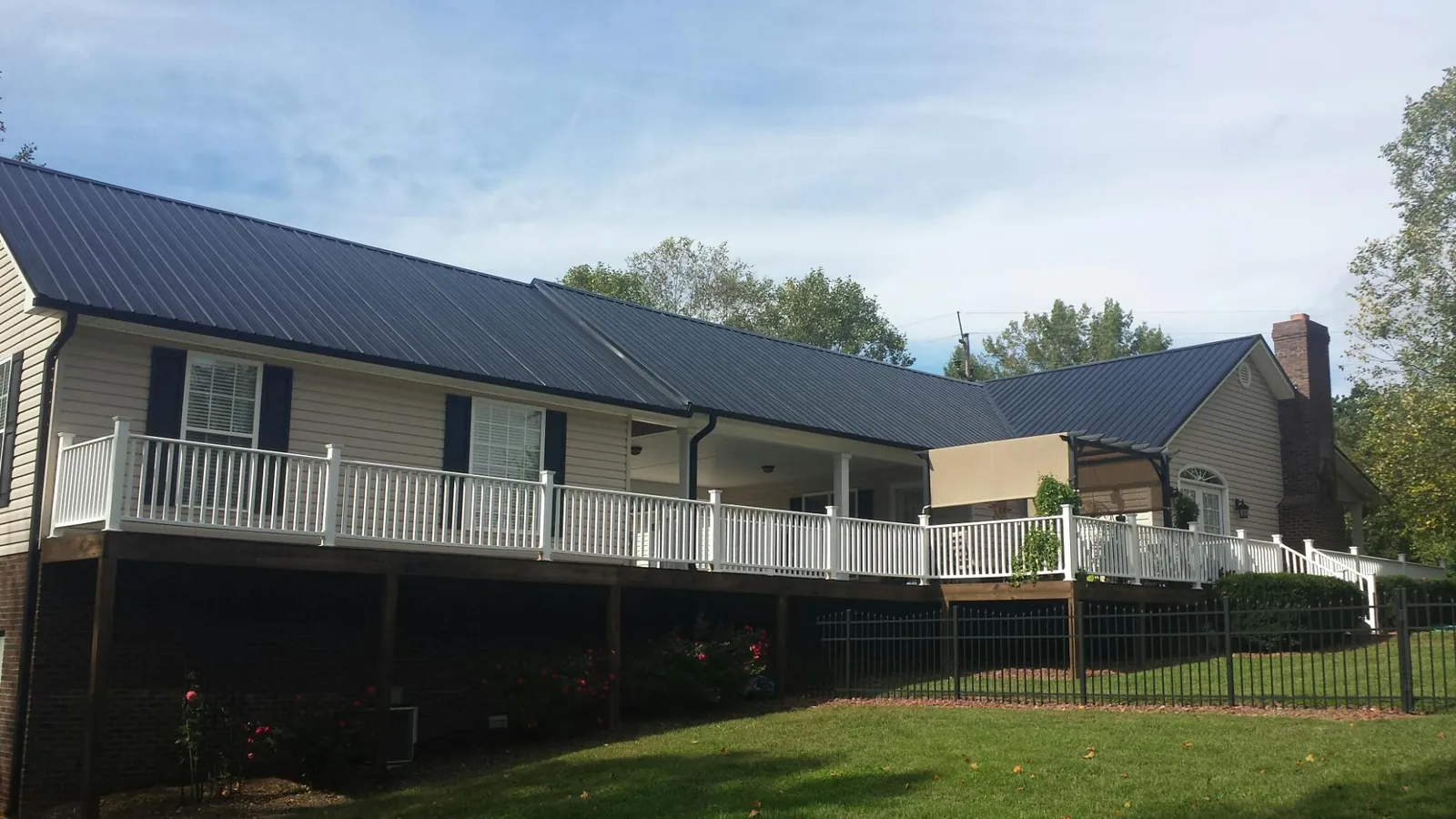Black metal roof above a long white railed deck on a hillside home in Forest