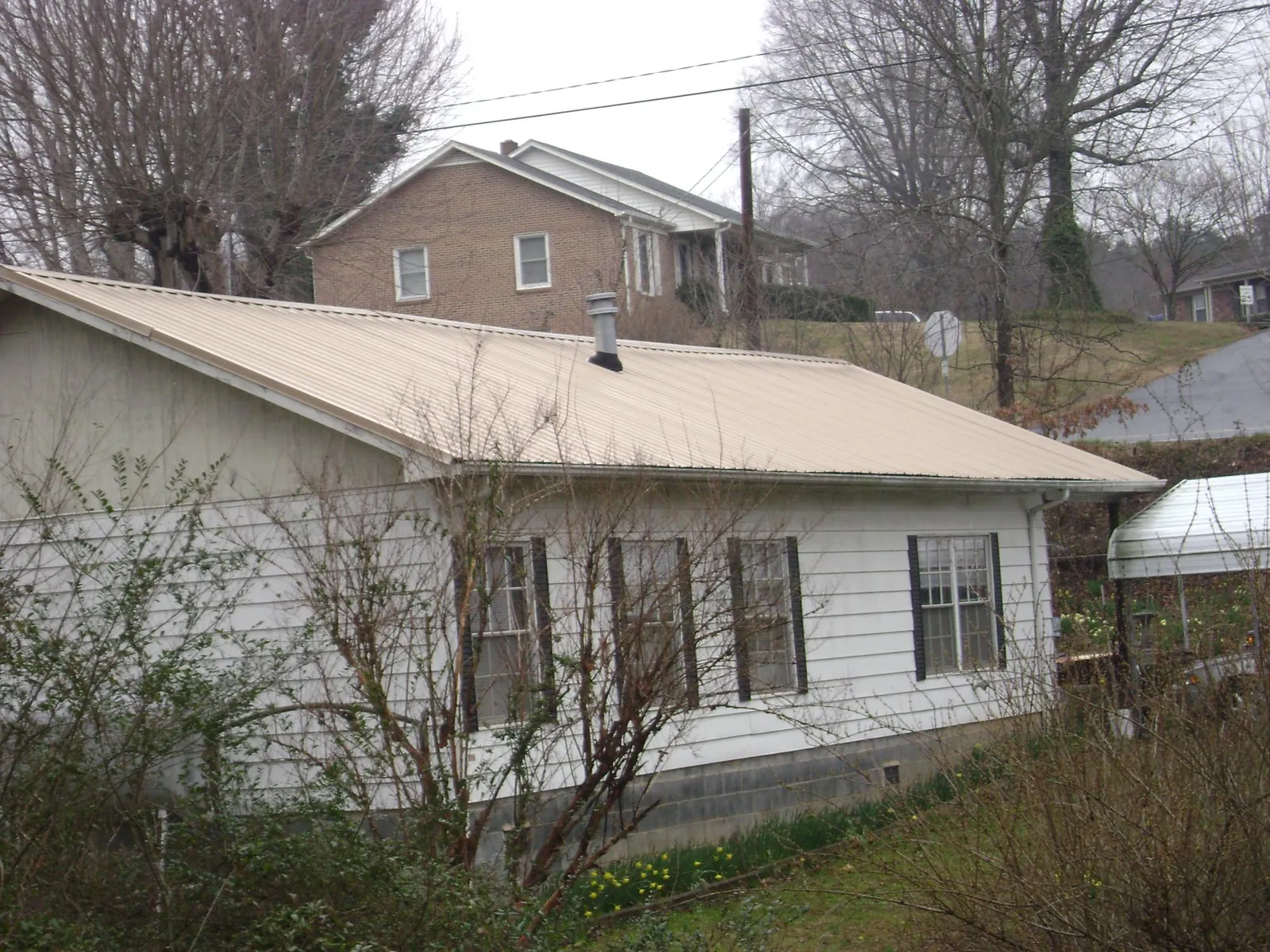 Tan metal roof on a white sided house set into a hillside — Commercial Roofing by Roofing Brothers in Forest