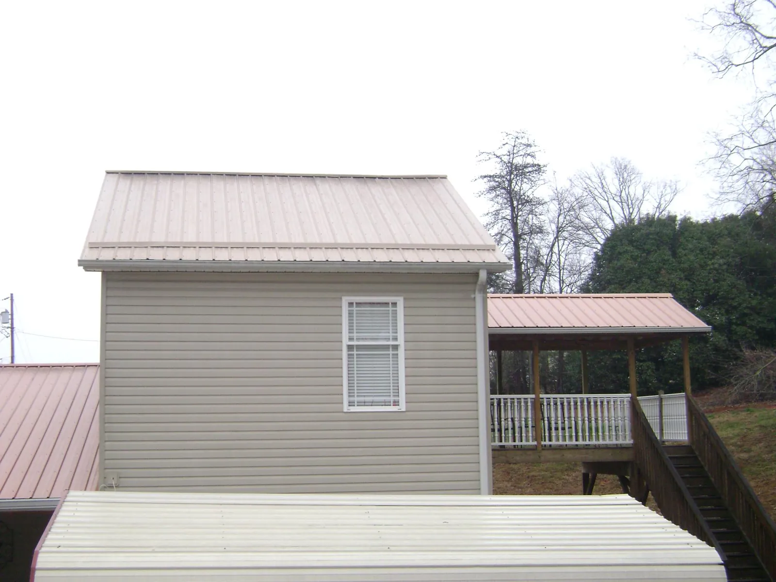 Tan metal roofs on a two story addition and attached porch, from a Roof Replacement job in Forest